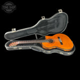 Acoustic guitar in a hard case with 'Tone Shop' logo in the corner.