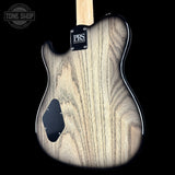 Close-up of the back of an electric guitar body with a natural wood grain finish, black pickguard, and PRS Guitars logo badge on a black background.
