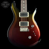 A close-up of an electric guitar body showing a metallic red-to-brown gradient finish, dual humbucker pickups, and control knobs against a black background. A Tone Shop watermark is visible in the top-left corner.