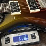 A close-up of a guitar body resting on a digital scale, showing the scale reading 7.146 oz.