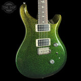 A close-up of a green glitter electric guitar body with a dark fretboard and silver hardware, shown against a black background with a Tone Shop watermark in the top left corner.