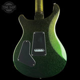 Close-up of the back of a double-cutaway electric guitar body with a dark green to black glitter finish and a bright green glow along the edge, shown against a black background. A Tone Shop watermark is visible in the top-left corner.