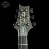 Close-up of a dark wood electric guitar headstock with six black tuning pegs, a white script signature, and the word 'Custom' printed vertically, shown against a black background with a Tone Shop watermark in the top left.