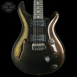 A close-up studio shot of an electric guitar body against a black background, featuring a metallic gold and black glitter finish with a white accent stripe. A Tone Shop watermark is visible in the top-left corner.