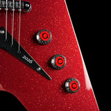 Close-up of a red glitter electric guitar body with three black and red control knobs, a black pickguard marked 2026, and part of the bridge and strings visible against a black background.
