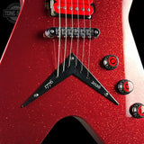 Close-up of a red glitter electric guitar body with a black V-shaped pickguard, chrome hardware, and red-and-black control knobs against a dark background.