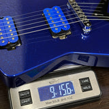 A close-up of a blue electric guitar body with blue pickups resting on a digital scale displaying 9 lbs 156 oz.