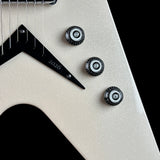 Close-up of a guitar body with a glittery champagne-gold finish, black pickguard, three black control knobs, and a black triangular string tree. The body has fine silver glitter throughout and the pickguard is engraved with the year 2026.