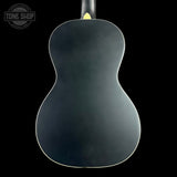 The back of a dark gray acoustic guitar against a solid black background, featuring a white edge trim and a yellow label at the neck joint. A Tone Shop watermark is visible in the top left corner.