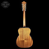 The back of a wooden acoustic guitar, showing the polished wood grain and six tuning pegs, photographed against a solid black background with a Tone Shop watermark in the top left corner.