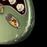 Close-up of a green guitar with worn finish and control knobs on a black background