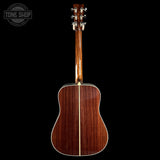 Acoustic guitar with a dark wood finish on a black background, featuring the Tone Shop logo.