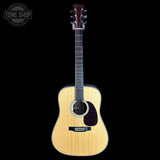 A natural wood acoustic guitar with a dark reddish-brown pickguard and black headstock, shown against a solid black background with a Tone Shop watermark in the top-left corner.