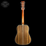 The back of an acoustic guitar with a rich wood grain finish, shown against a solid black background with a Tone Shop watermark in the top left corner.