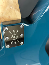 Close-up of a blue guitar with a metal block featuring a logo on the neck