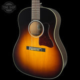 A classic acoustic guitar with a sunburst finish, featuring a dark black outer body fading to a warm amber-orange center, with a dark reddish-brown pickguard and white binding, shown against a solid black background.