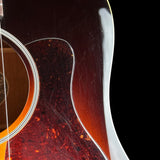 Close-up of an acoustic guitar body showing a dark brown sunburst finish, a tortoiseshell-style sound hole surround, and a white edge trim against a black background.