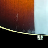 Close-up of the lower edge of a guitar body showing a dark brown sunburst finish, a light cream binding edge, and a silver tailpiece against a black background.