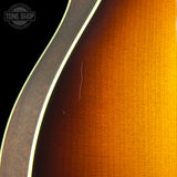 Close-up of an acoustic guitar body showing the sunburst finish transitioning from black to amber brown and bright yellow-gold, with a white edge stripe and a visible Tone Shop watermark in the upper left.