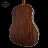 Close-up of the back of an acoustic guitar showing a rich dark brown wood grain finish and white binding, set against a solid black background with a Tone Shop watermark in the top left.