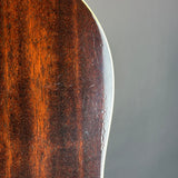 Close-up of a polished wooden object, likely a guitar body, showing a rich dark brown wood grain finish and a light-colored edge against a neutral gray background.
