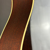 Close-up of the back of an acoustic guitar showing a dark brown wood finish and a cream-colored binding edge.