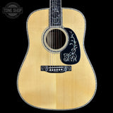 Acoustic guitar with decorative inlay on a black background, featuring the Tone Shop logo.