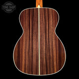 Back view of a wooden acoustic guitar with a visible brand logo in the corner.