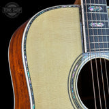Close-up of an acoustic guitar's soundhole and wooden body on a black background with 'Tone Shop' logo.