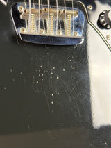 Close-up of a guitar's bridge and strings with a worn black finish.