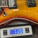 Guitar being weighed on a digital scale with a blue display.