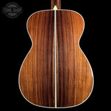 The back of an acoustic guitar made of rich, dark brown wood with a light cream center stripe, shown against a solid black background. A Tone Shop watermark is visible in the top-left corner.