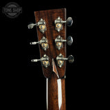 Close-up of a guitar headstock with six tuning pegs and ornate gold-toned hardware on a dark wood finish, shown against a black background with a Tone Shop watermark in the top left.