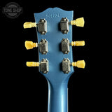 Close-up of a blue guitar headstock with yellow tuning pegs on a black background, featuring 'Tone Shop' branding.