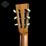Close-up of the headstock of a wooden acoustic guitar against a solid black background, showing the six tuning pegs and a Tone Shop watermark in the top left corner.