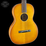 A classic acoustic guitar with a natural sunburst finish, shown from the front against a solid black background. The Tone Shop logo is visible in the top-left corner.