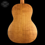 The back of a wooden ukulele or small guitar made from a single natural wood tone, shown against a solid black background with a Tone Shop watermark in the top left corner.