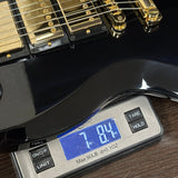Digital scale displaying weight of a black electric guitar on a wooden surface