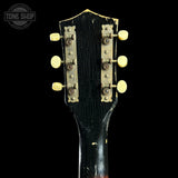 Close-up of a guitar headstock with tuning pegs on a black background, featuring 'Tone Shop' logo.