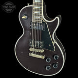 Electric guitar with a dark finish on a black background, featuring the Tone Shop logo.