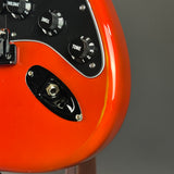Close-up of an electric guitar body in a bright orange finish, showing part of the black control panel with volume and tone knobs and a black pickup cover.
