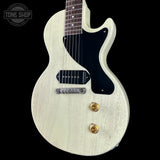 White electric guitar with a black pickguard on a black background, featuring the Tone Shop logo.