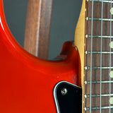 Close-up detail of an electric guitar showing the glossy red body, black pickguard, maple neck, and dark fretboard.