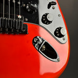 Close-up of a red electric guitar body showing the black pickguard, control knobs, bridge, and part of the neck against a dark gray background.