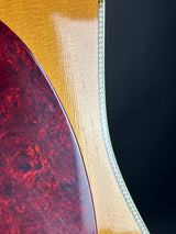 Close-up of a guitar's wooden neck and red tortoiseshell fretboard against a dark background