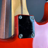 Close-up of the rear corner of a red electric guitar body, showing a black rectangular plate secured with four silver screws, alongside the natural wood neck and dark background.