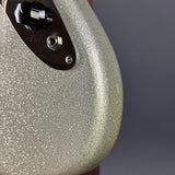 Close-up of a glittery silver electric guitar body with a black control plate and silver hardware, set against a dark gray background.