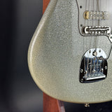 Close-up of a Fender electric guitar body in a metallic silver glitter finish, showing part of the pickguard, bridge, and strings against a dark background.
