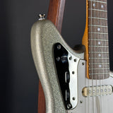 Close-up of a glittery metallic silver electric guitar body with a black pickguard, white trim, and part of the wooden fretboard.