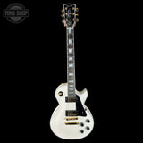 White electric guitar with gold hardware on a black background, featuring 'Tone Shop' logo.